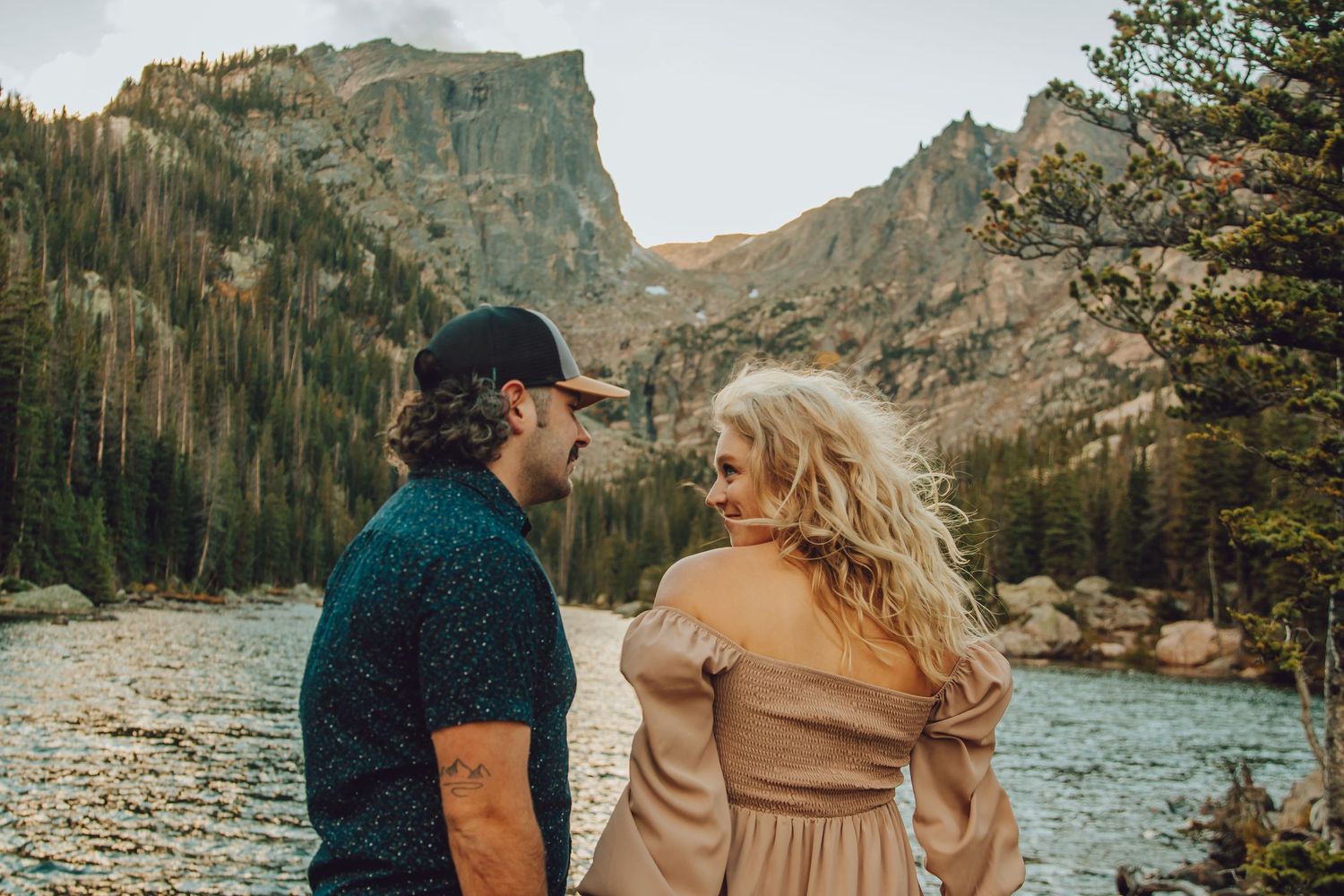 Couple enjoying a romantic moment by a scenic mountain lake surrounded by evergreen forest and rocky cliffs.