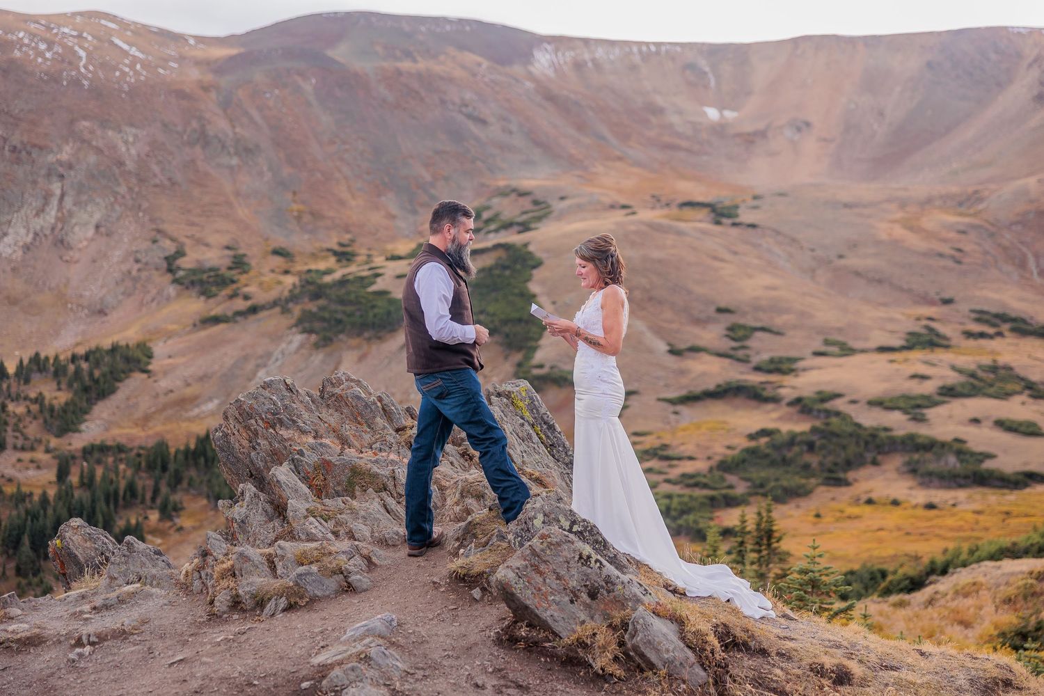 A couple stands at the edge of a scenic mountain vista with dramatic desert landscape stretching into the distance in Estes Park