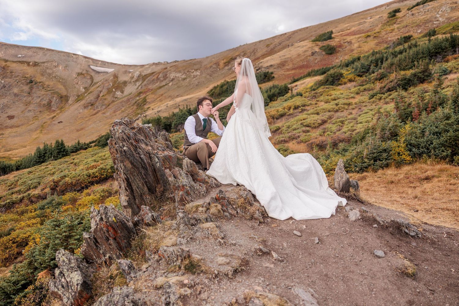 A flowing white wedding dress billows dramatically against a rugged mountain landscape during a beautiful sunset in Rocky Mountain National