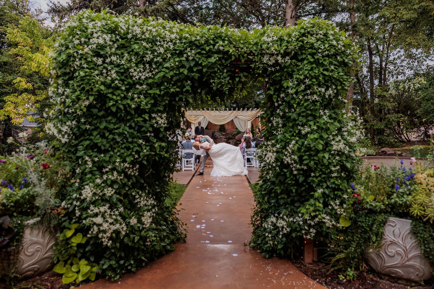 A winding brick pathway leads through a lush garden with green foliage and trees on both sides.
