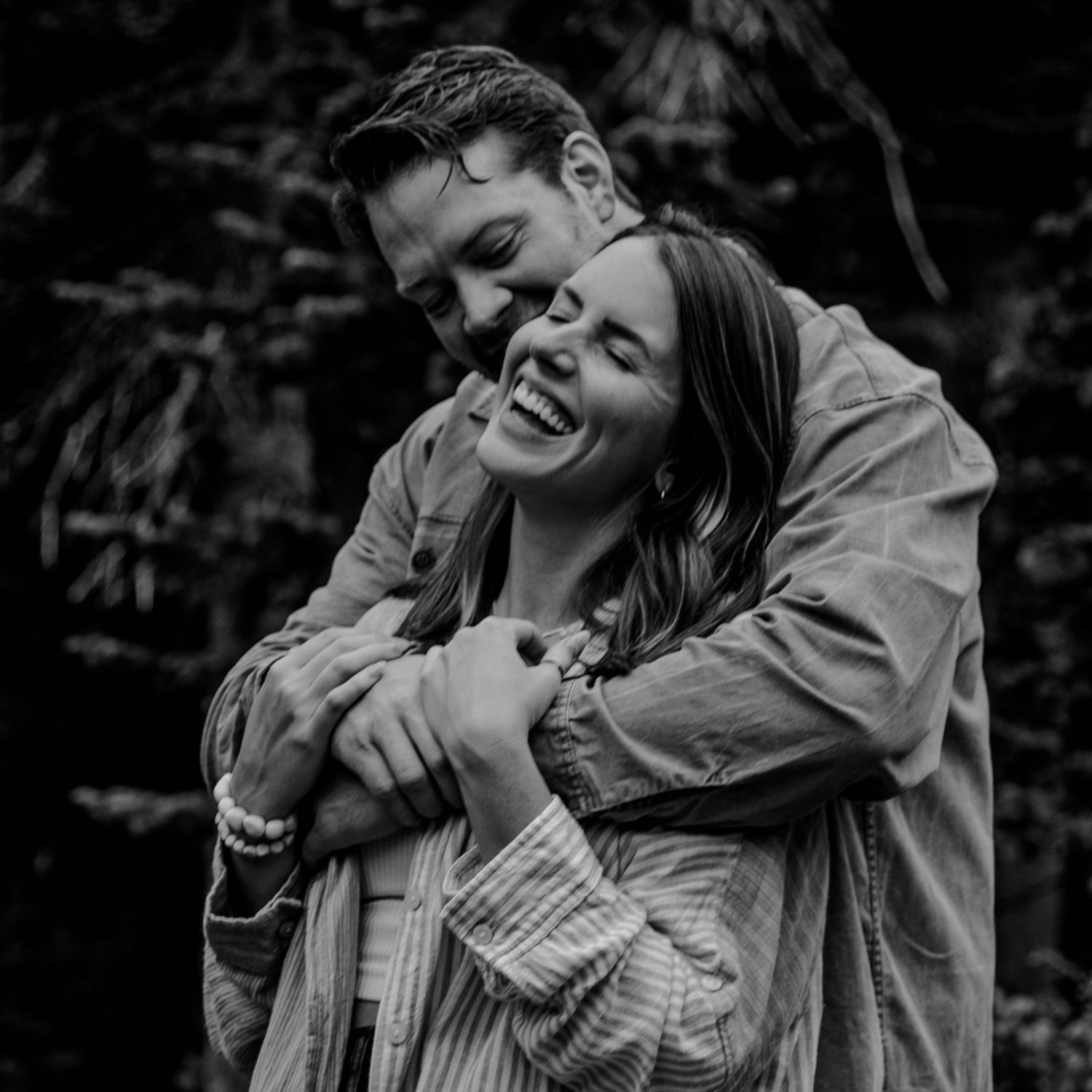 Black and white photograph showing a playful embrace between two people sharing a joyful moment outdoors.