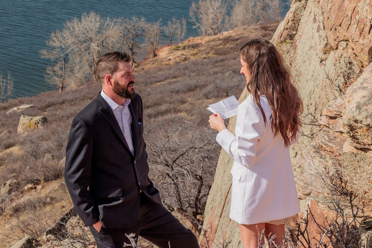 A couple shares a special moment on a scenic coastal cliff overlooking the ocean during a sunny day.