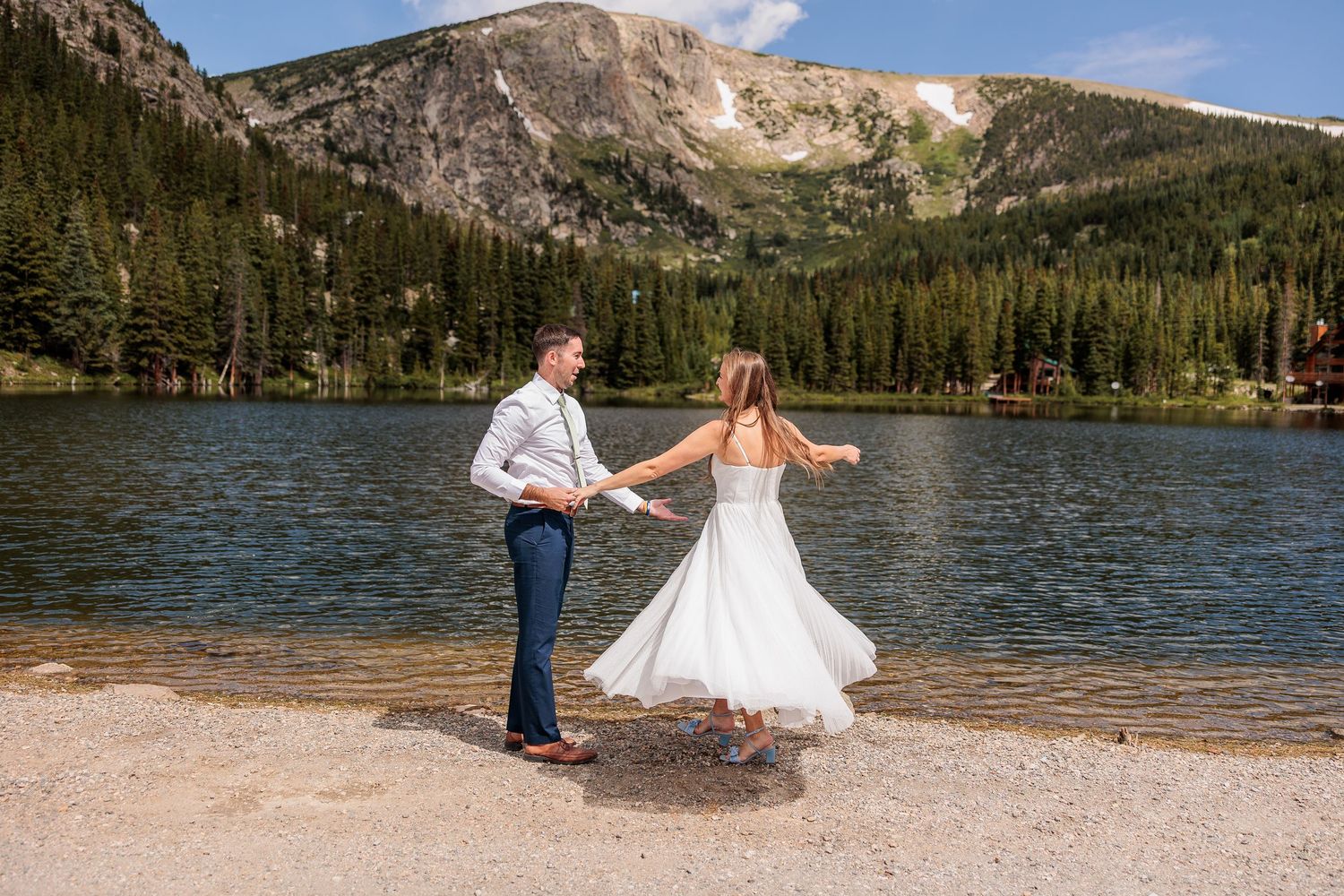 Scenic mountain lake wedding photo session with snow-capped peaks and evergreen forest in the background.