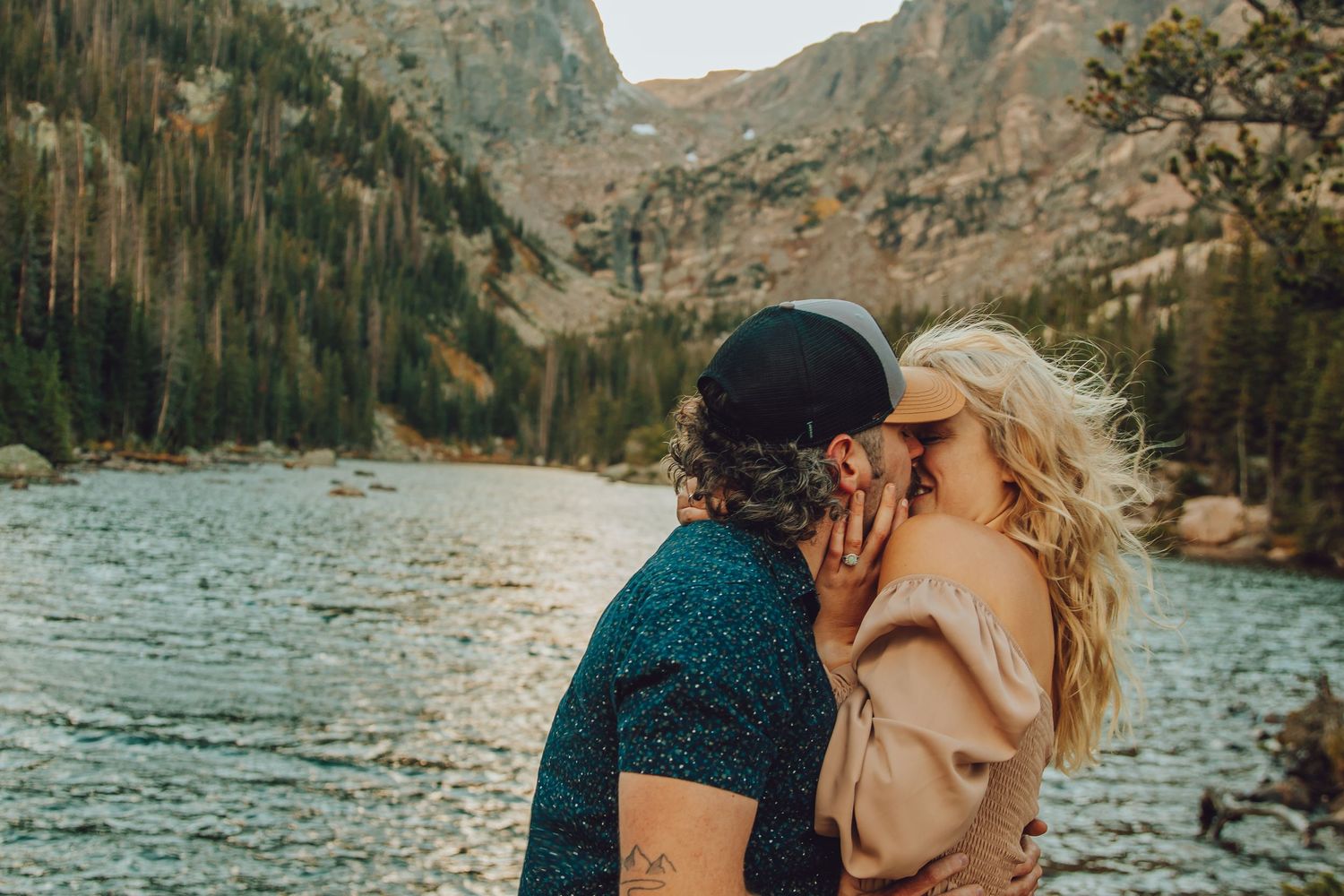 A couple shares an intimate moment by a turquoise mountain lake surrounded by rugged peaks and autumn foliage.