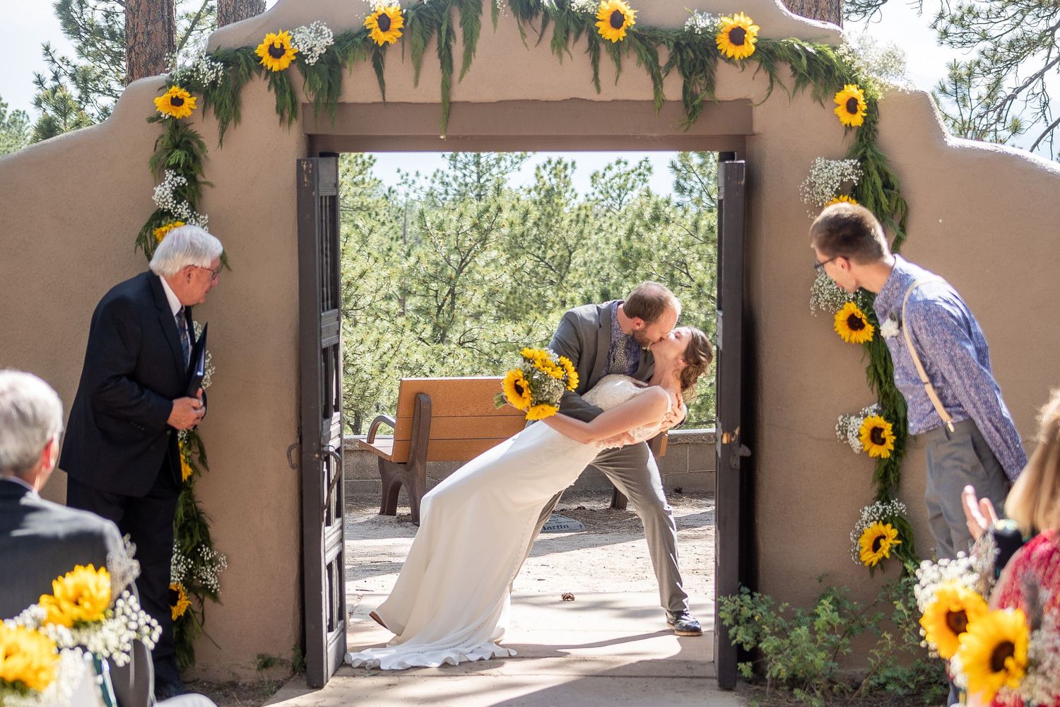 A wedding ceremony under an adobe archway decorated with bright sunflowers.