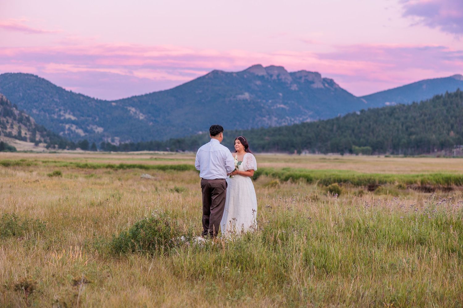 A romantic sunset moment in a mountain meadow with pink and purple skies overhead.