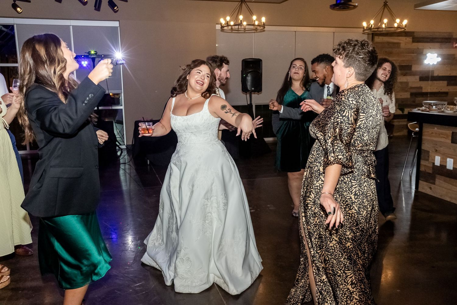 Wedding reception guests dancing and celebrating on the dance floor under chandeliers at an indoor venue.