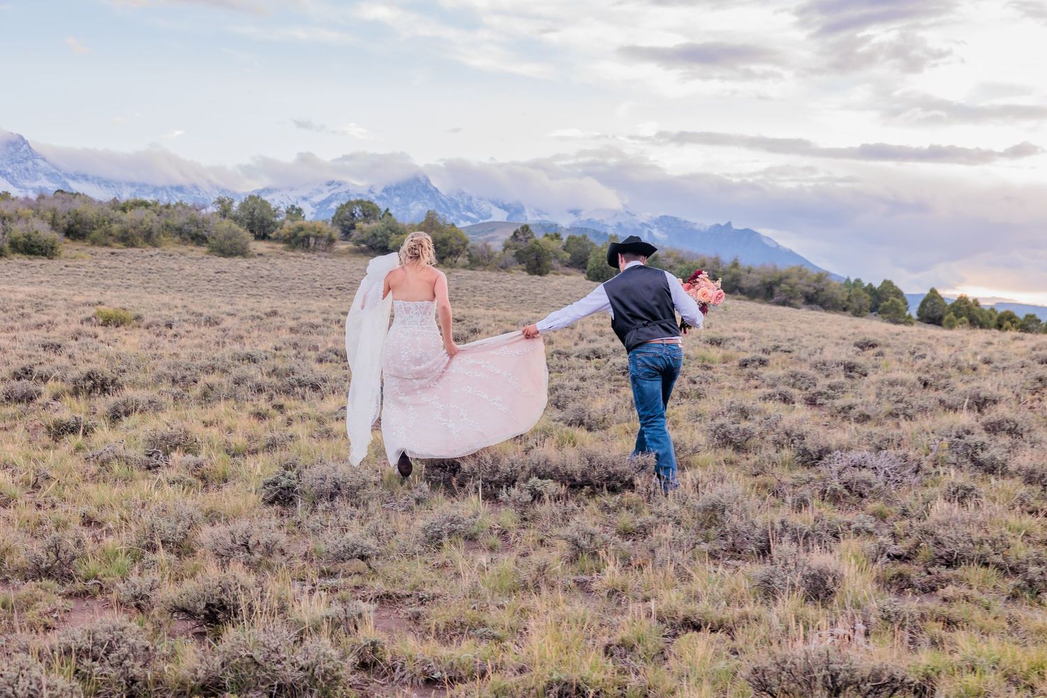 A couple walks together through a scenic mountain landscape at sunset holding hands in the desert terrain.