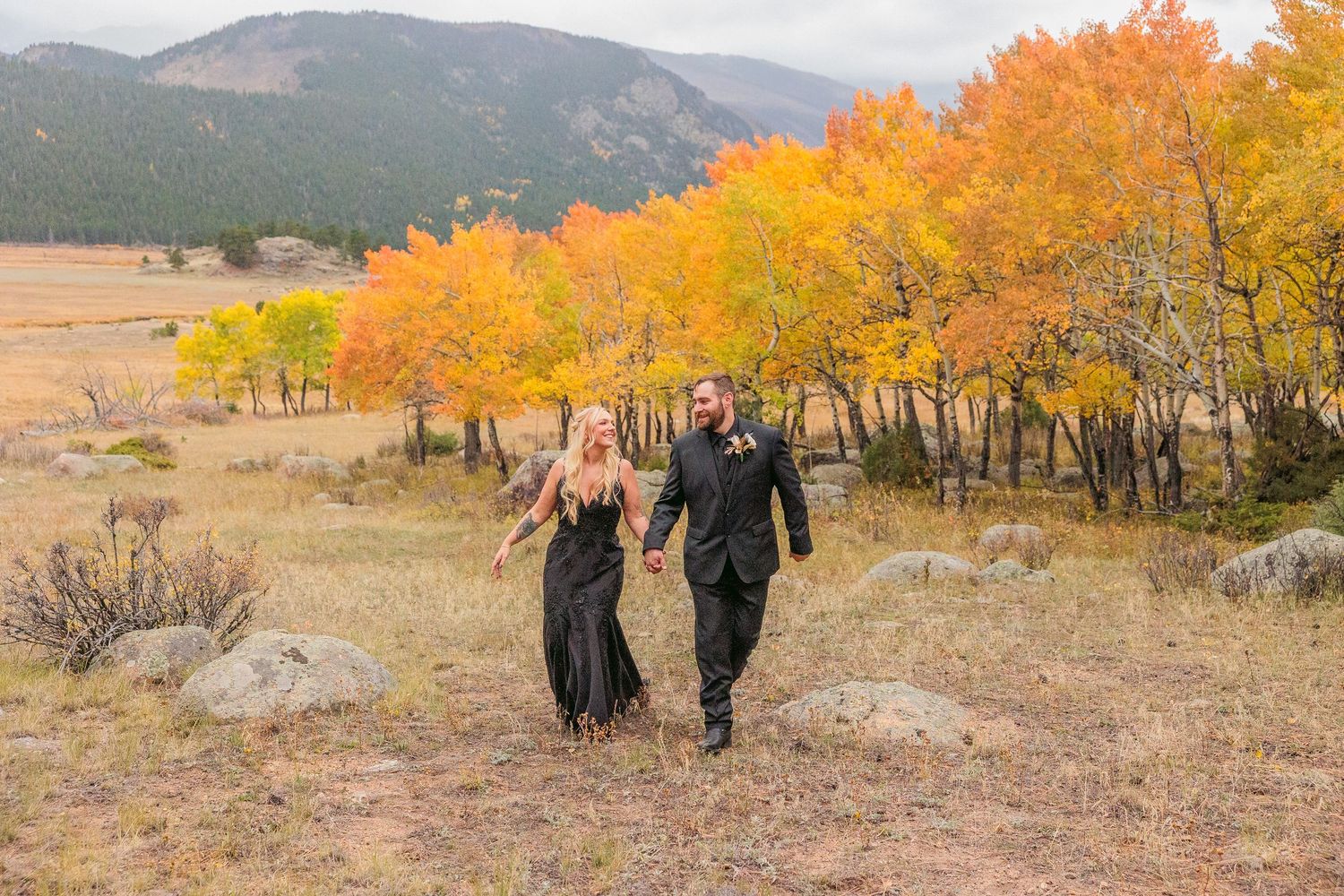 Couple walking together on a mountain trail surrounded by vibrant orange autumn foliage and rolling hills.