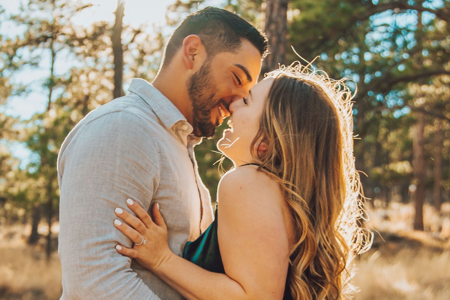A romantic couple embraces in a sun-drenched forest setting during a golden hour photoshoot.