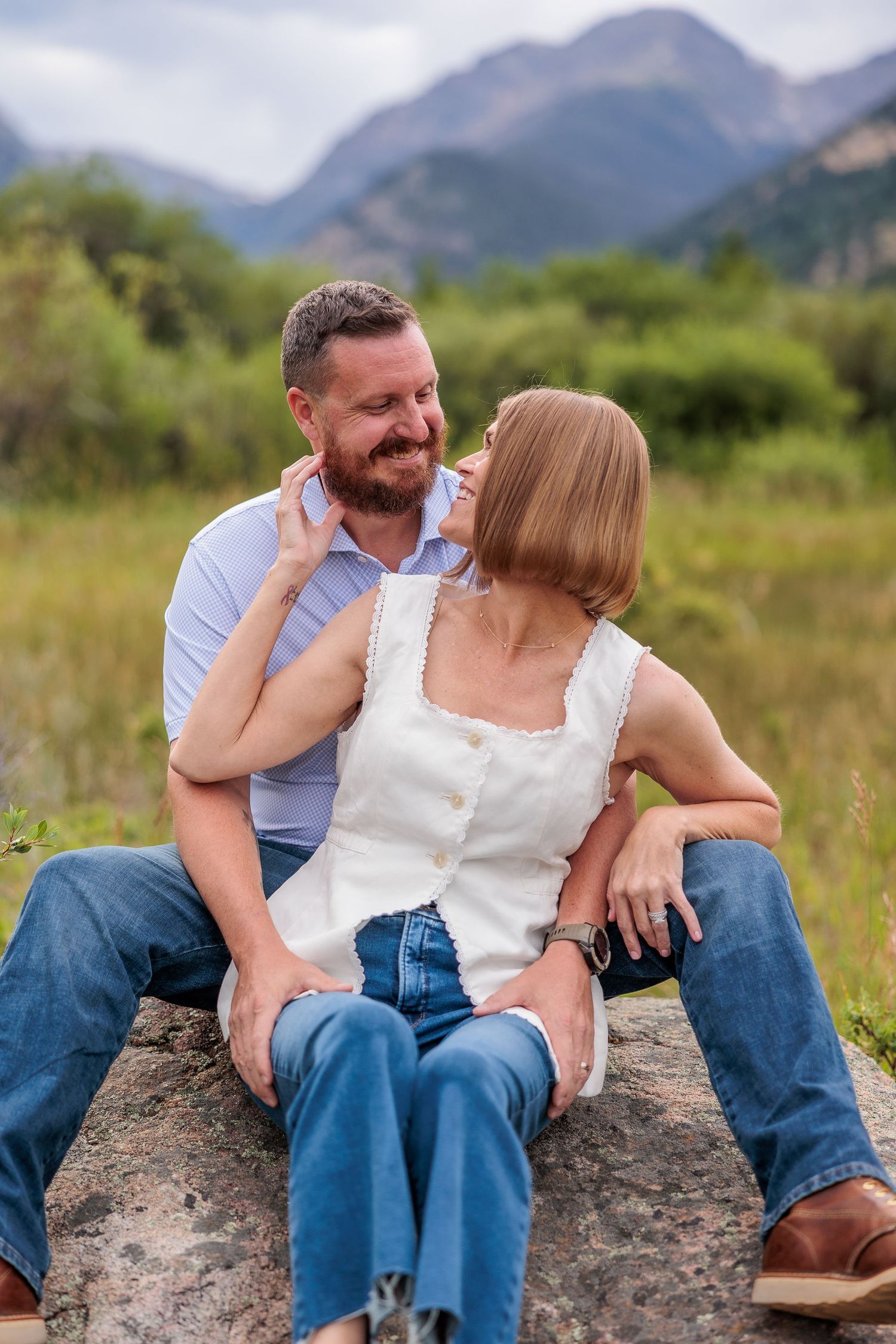 A couple sits close together on a rock in a mountain meadow, sharing intimate moments across four progressive shots.