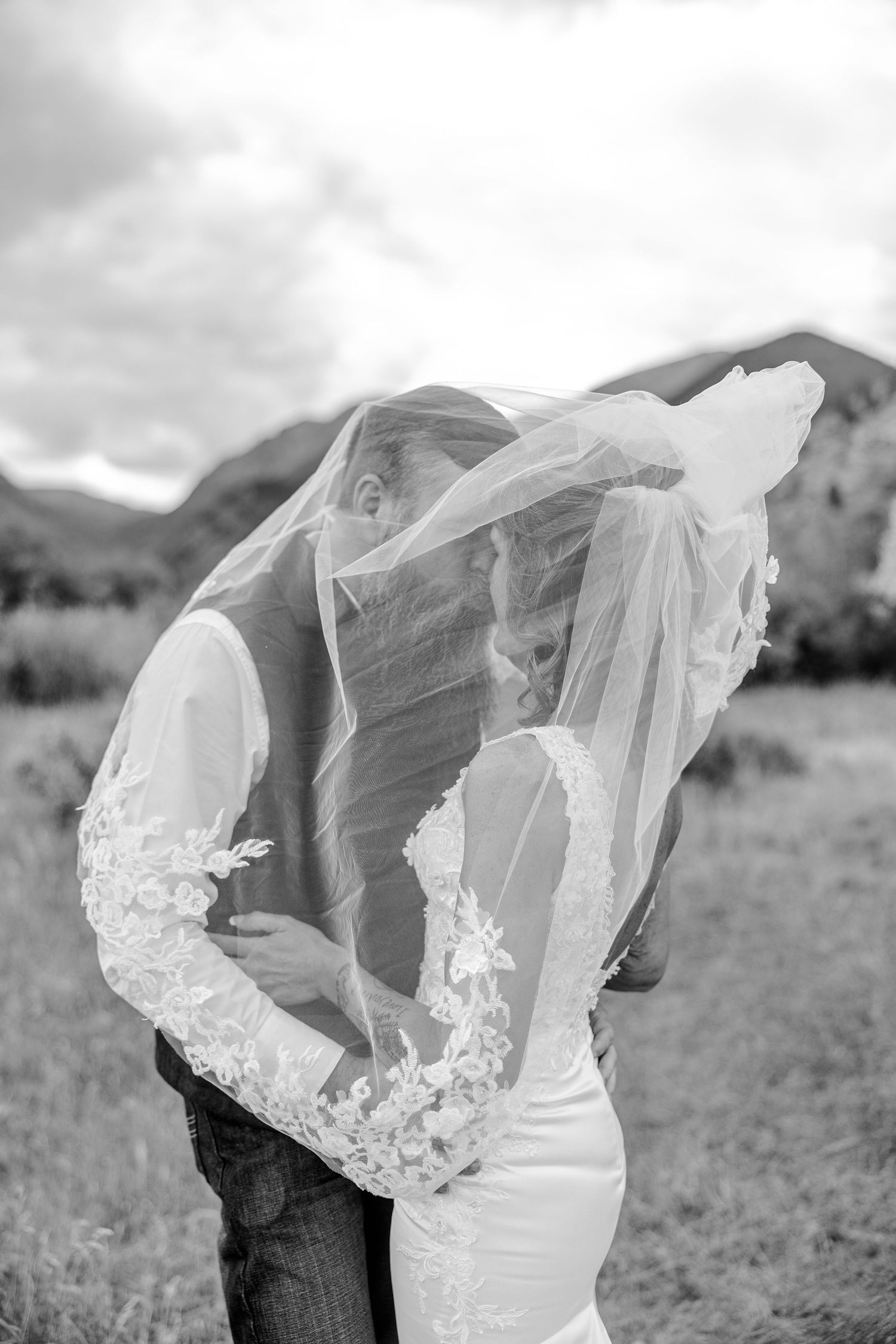A romantic black and white photograph shows a couple embracing while a delicate lace veil flows in the wind.