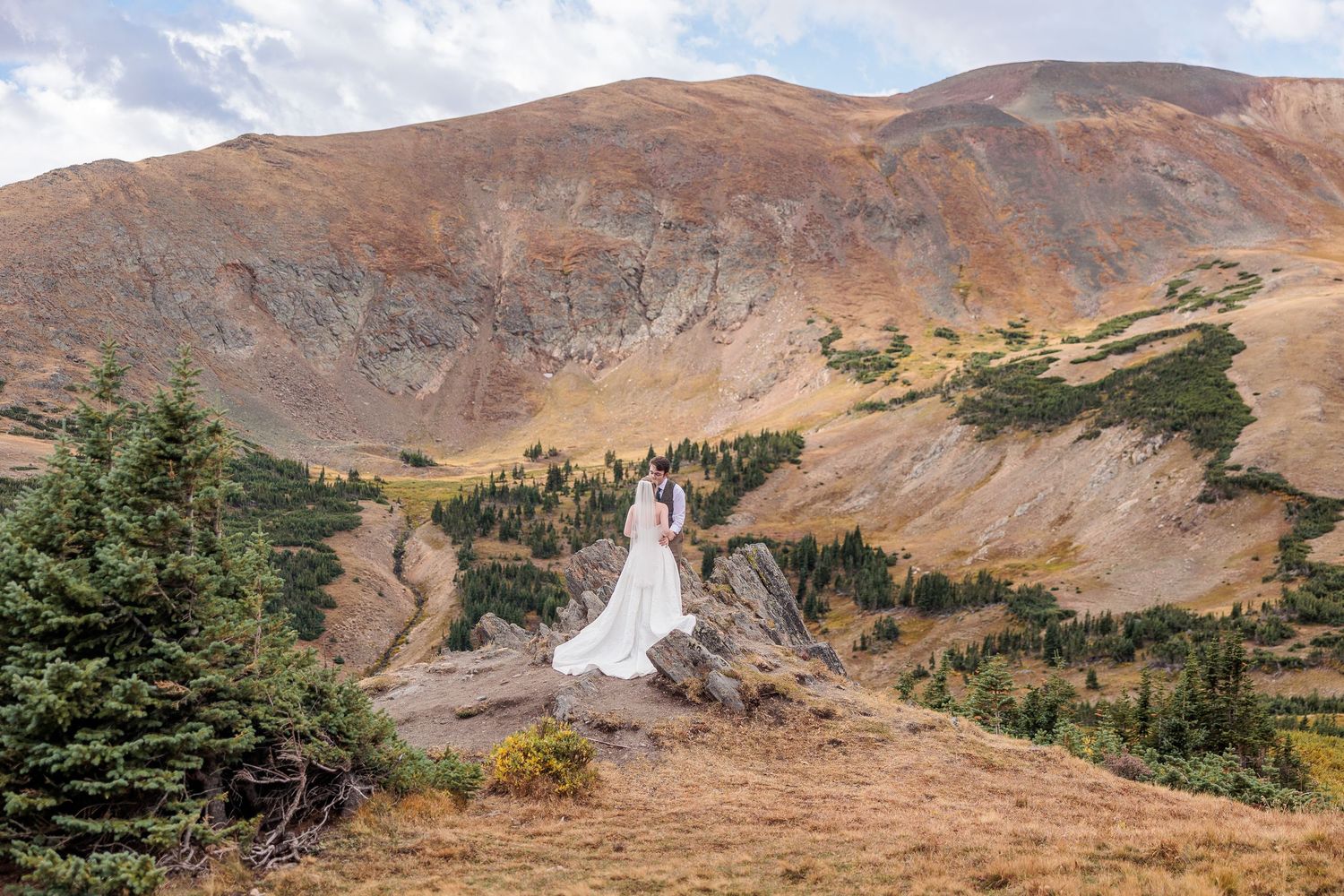 Wedding dress silhouette against dramatic mountain landscape with fall colors.