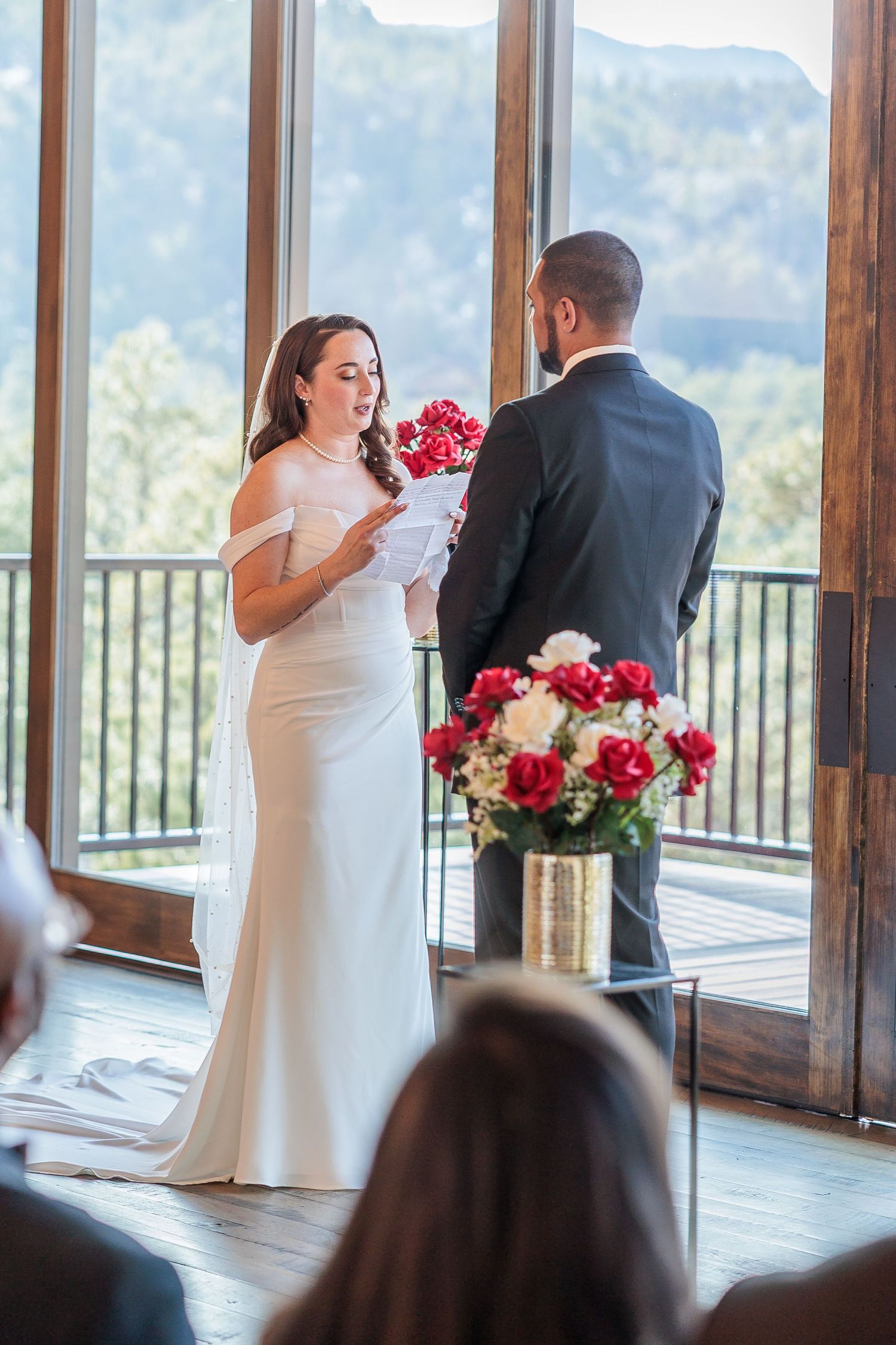 Wedding ceremony in a mountain venue with panoramic windows and red floral arrangements.