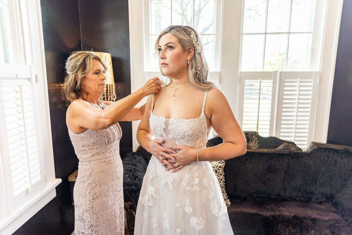 Two women in formal dresses making final adjustments before a wedding ceremony.