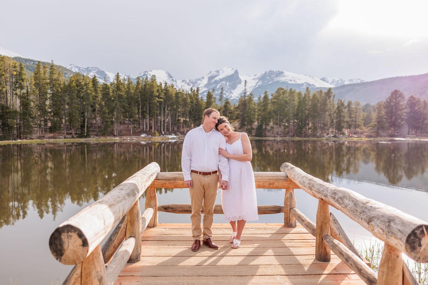 A couple shares a romantic moment on a wooden dock overlooking a mountain lake.