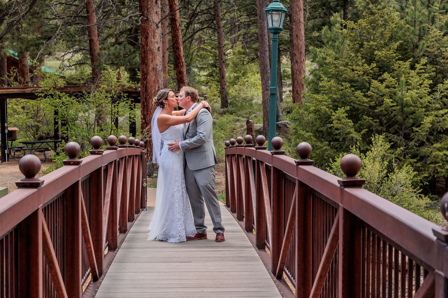 A couple shares a romantic moment on a rustic wooden bridge surrounded by lush green forest.