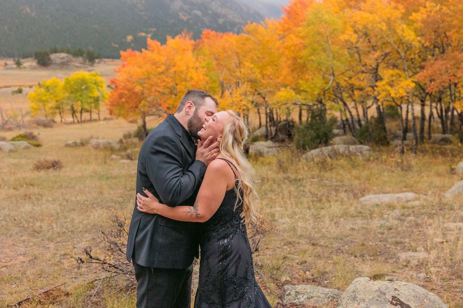 Couple embraces in a scenic autumn landscape with vibrant orange and yellow foliage in the background.