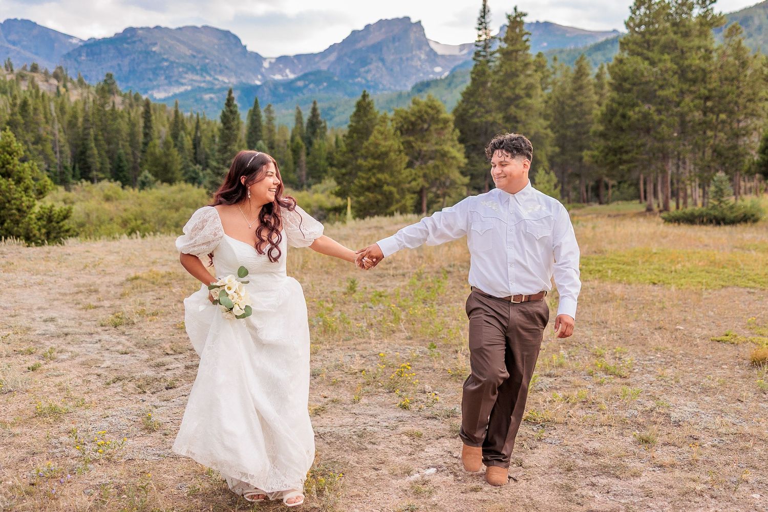 A couple shares a romantic moment in a scenic mountain meadow during their wedding photoshoot.
