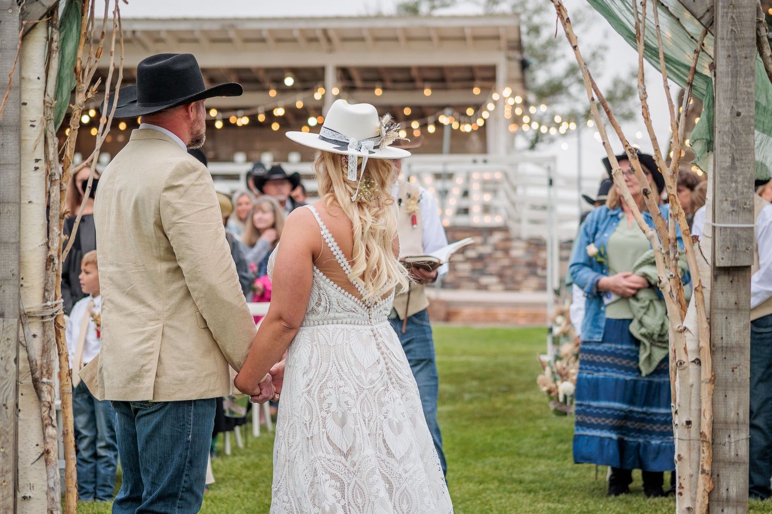 A couple celebrates their rustic outdoor wedding ceremony with guests gathered under string lights and wooden posts.