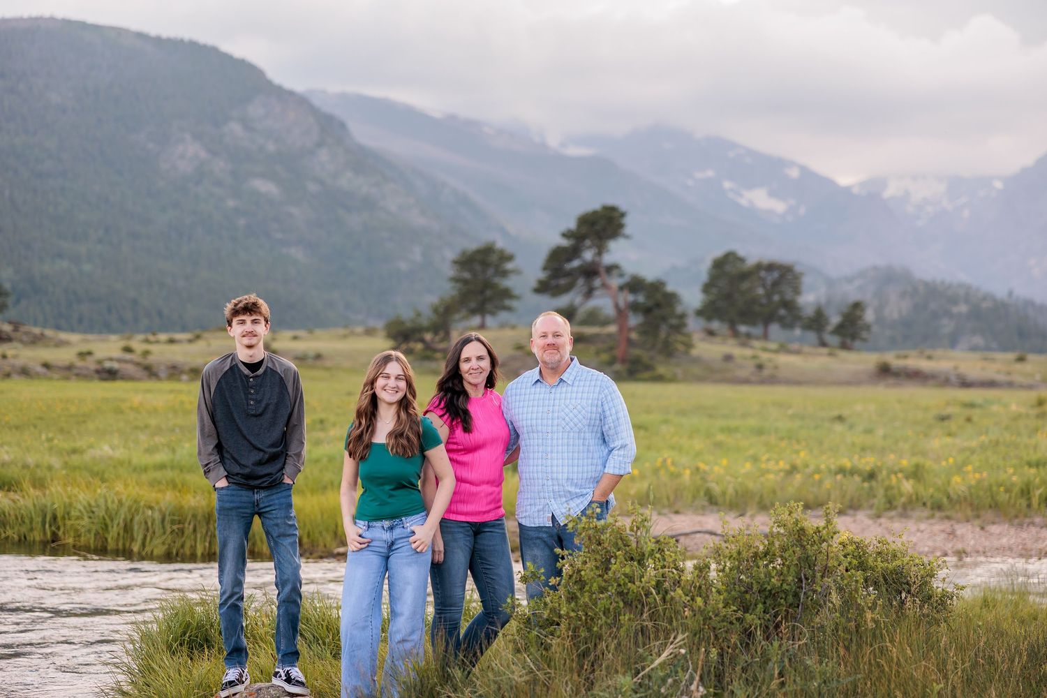 A group of people stand together against a backdrop of majestic mountains and green fields in Colorado.