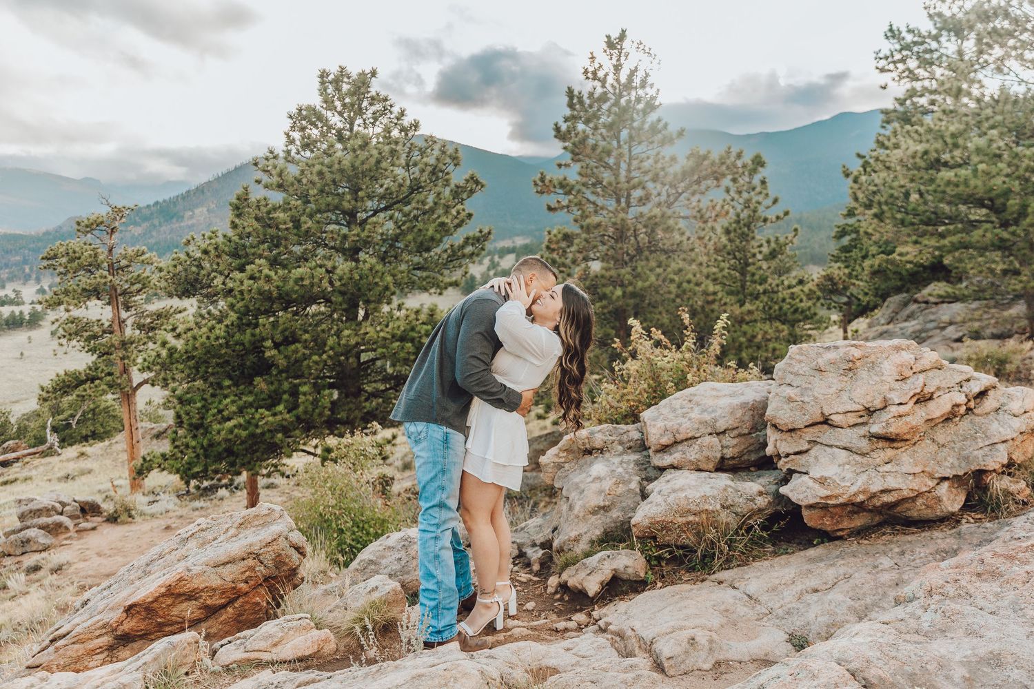 Rocky mountain overlook with pine trees frames scenic outdoor moment against mountain backdrop.