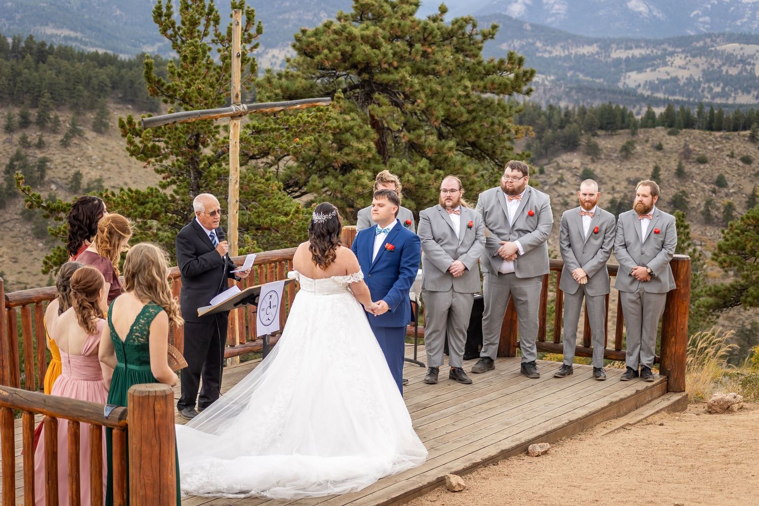 Mountain wedding ceremony takes place on wooden deck overlooking scenic valley with pine trees and distant peaks.