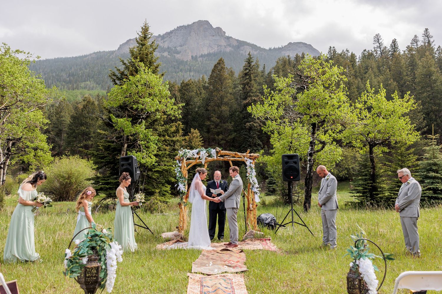 Outdoor mountain wedding ceremony in Colorado with rustic wooden arch and evergreen forest backdrop.