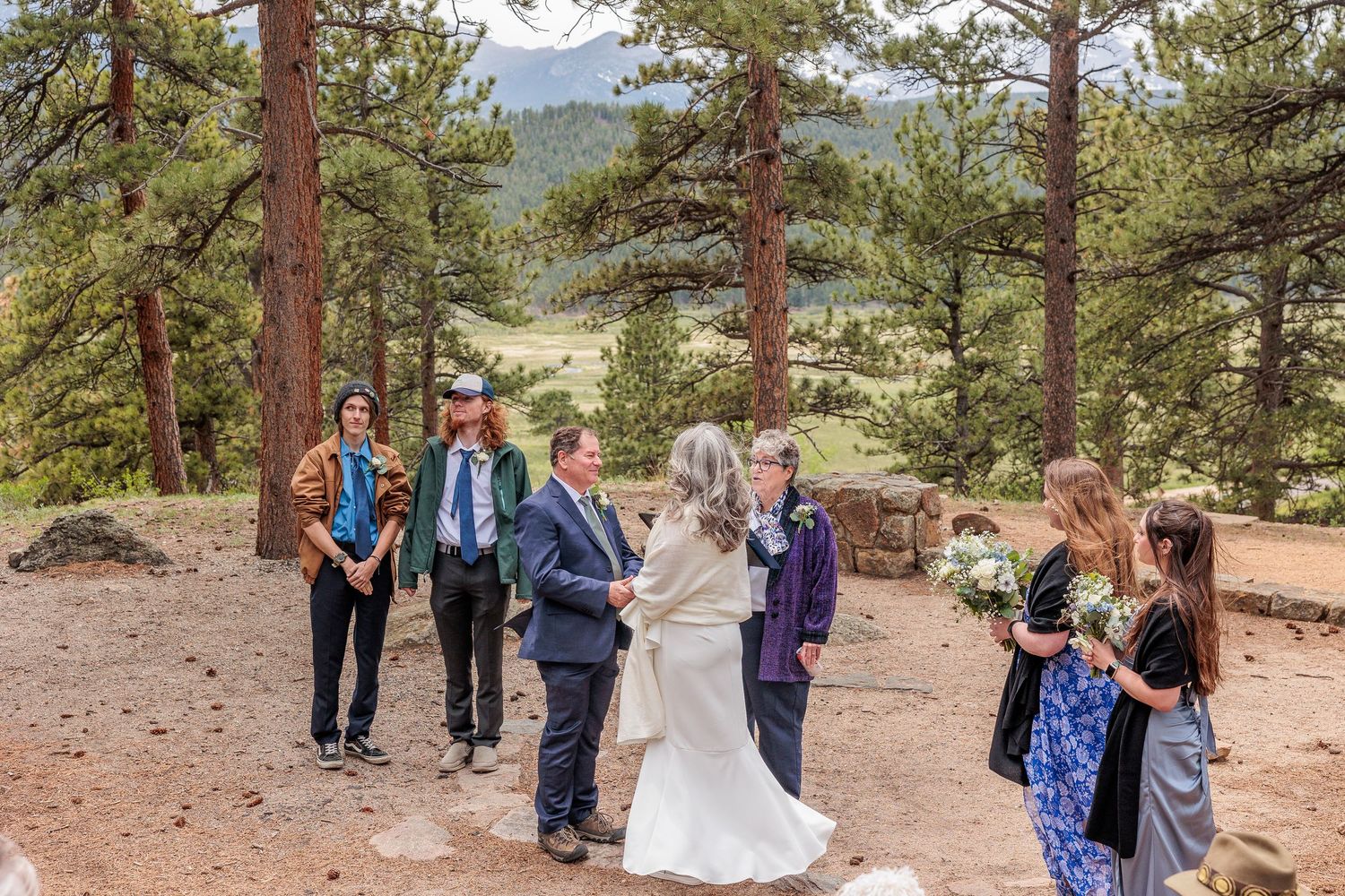 Wedding party poses together in a scenic mountain forest with tall pine trees.