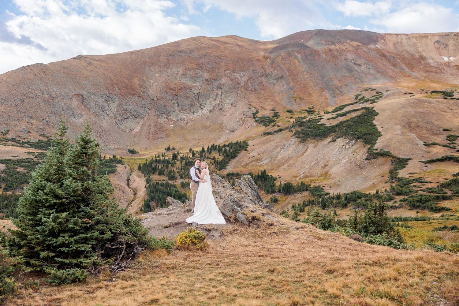 A panoramic view of rugged mountain terrain with brown hills and sparse vegetation stretches across the landscape.