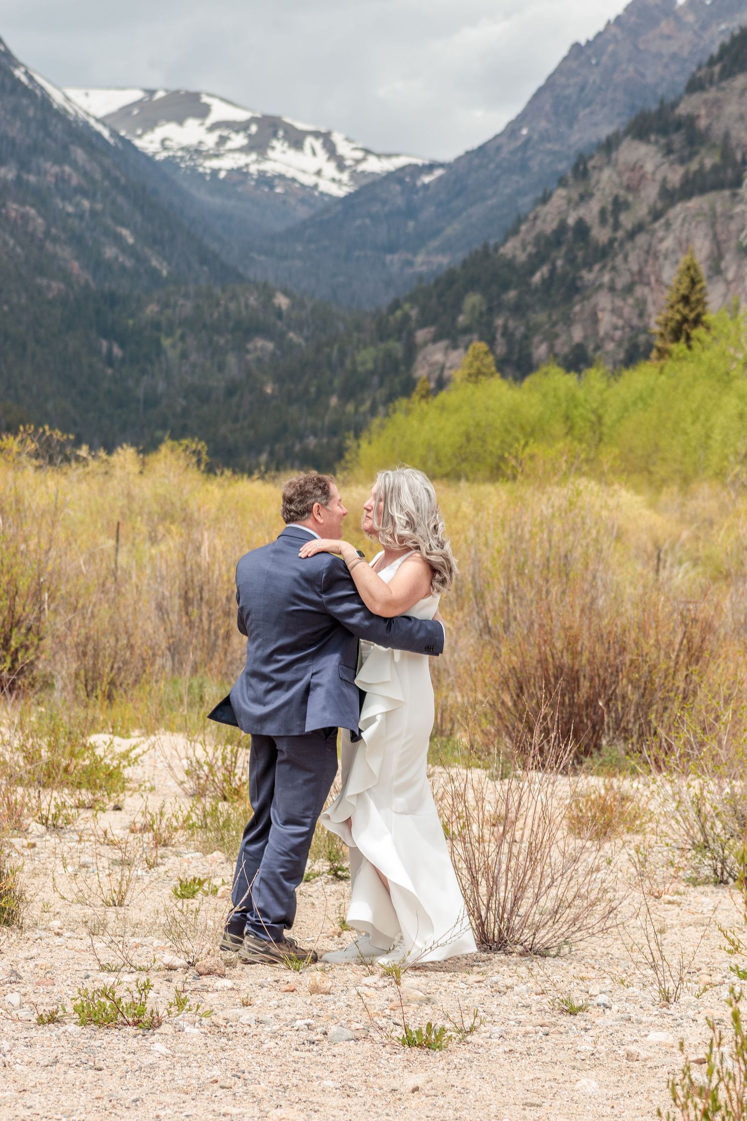 A couple shares a romantic moment in front of snow-capped mountains and desert brush in a scenic landscape.