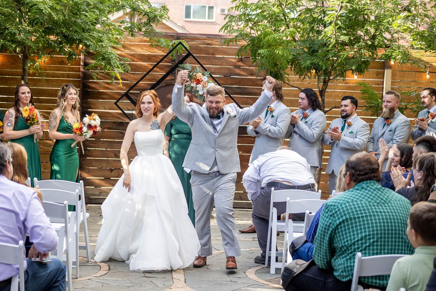Wedding party celebration with guests in casual attire dancing outdoors near rustic wooden walls.
