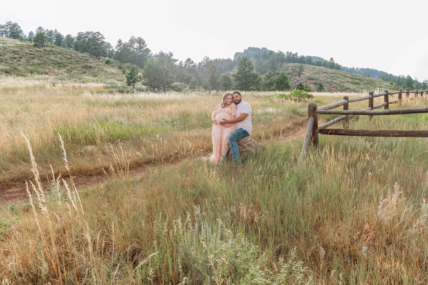 A scenic panoramic view of a rustic wooden fence stretching along a grassy hillside trail on a sunny day.