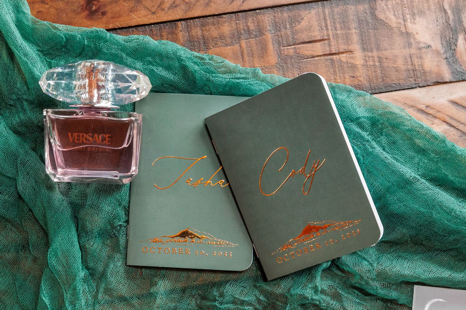 Luxury leather coasters and whiskey glass arranged on emerald green velvet fabric with gold lettering details.