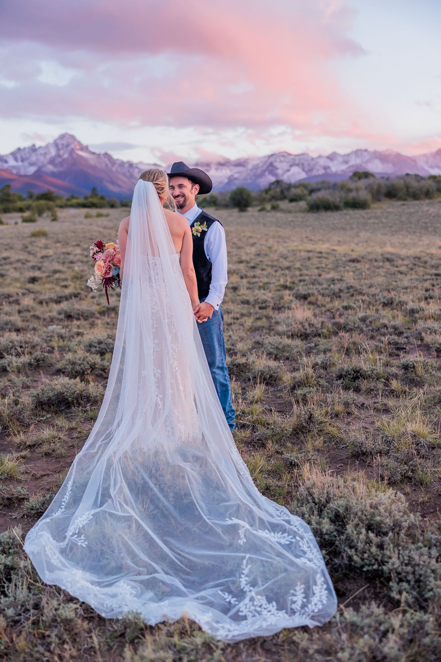 Romantic desert wedding portraits with flowing veil against pink mountain sunset.