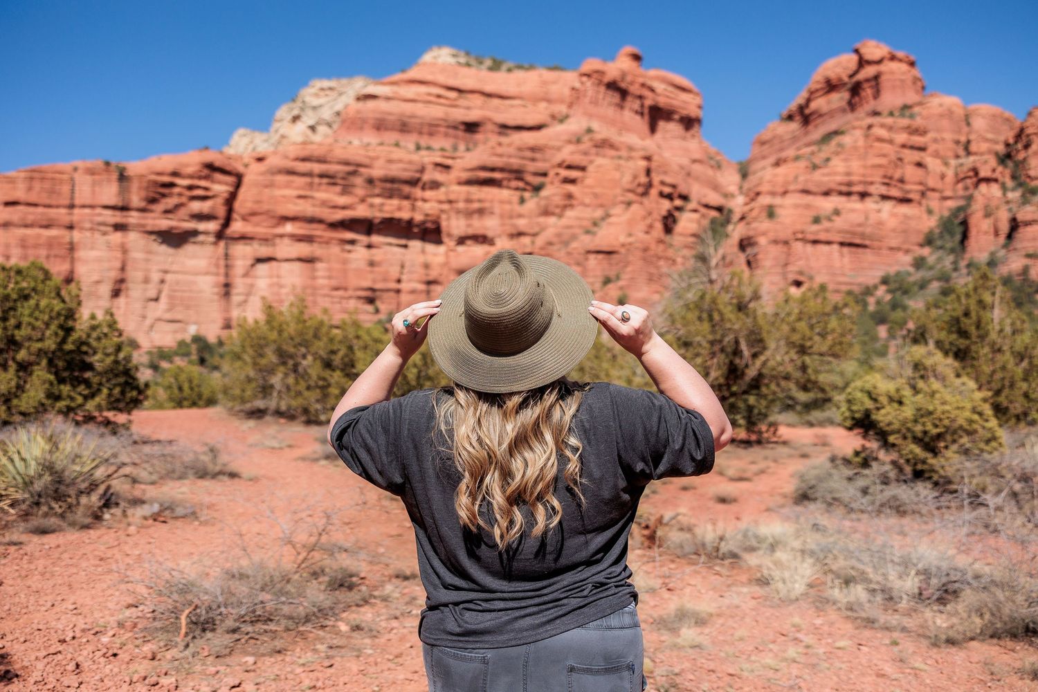 Someone wearing a brown hat and dark shirt admires the red rock formations in a desert landscape.