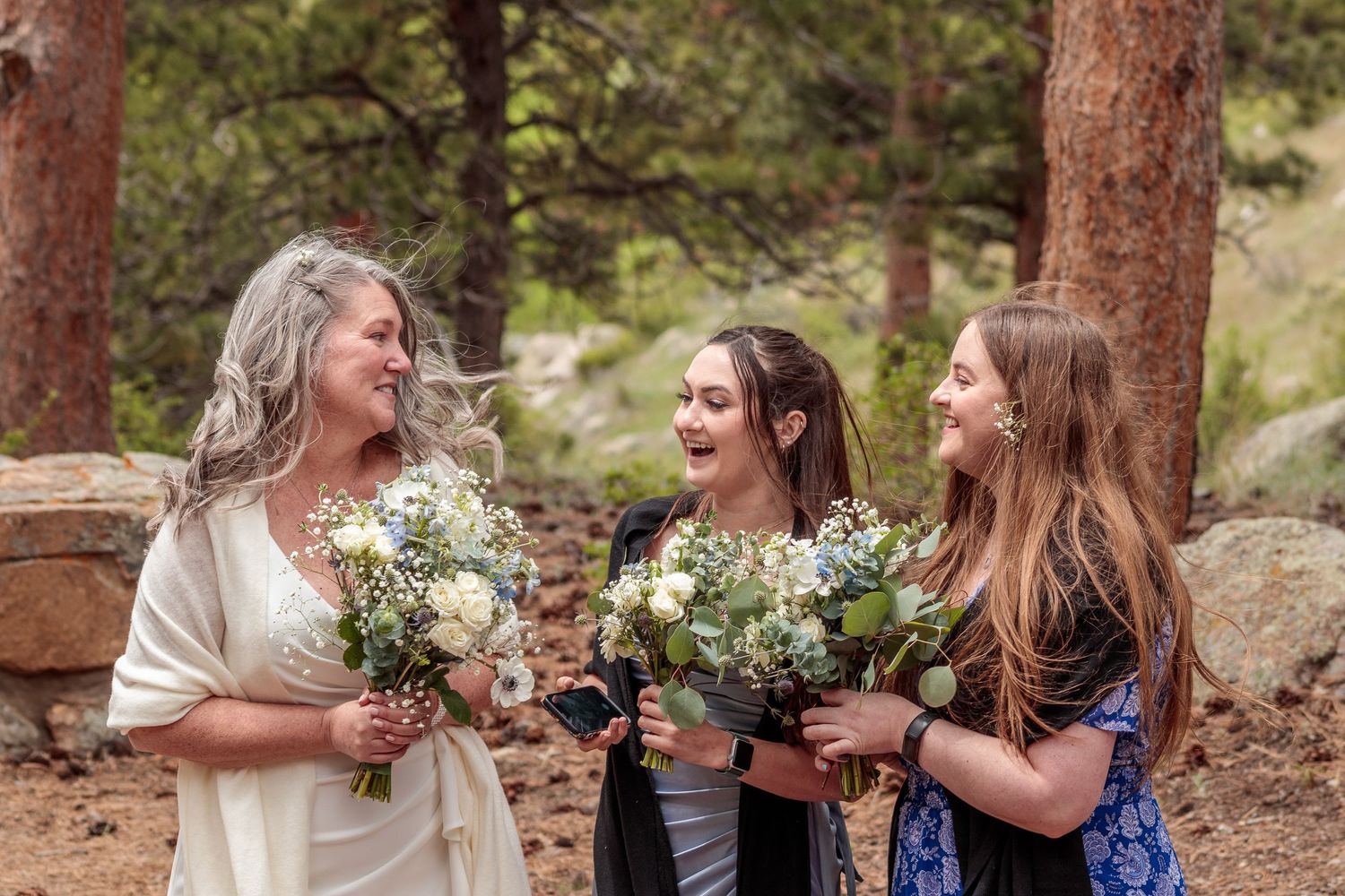 Joyful wedding party sharing laughs and embraces among tall pine trees in an outdoor forest setting.