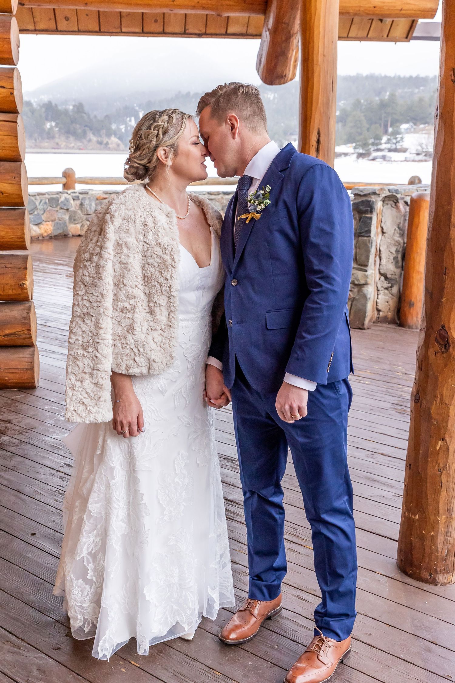 A romantic wedding moment on a rustic covered deck overlooking a misty lake, with elegant white lace and navy blue attire.