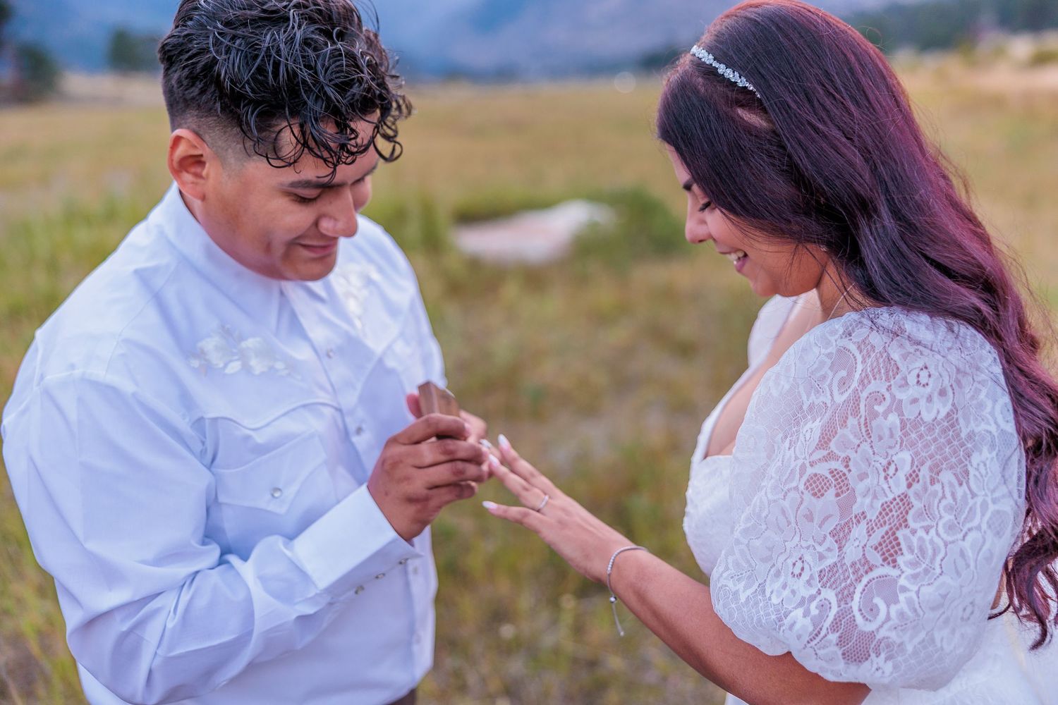 A couple in wedding attire dances together in an outdoor field during golden hour.