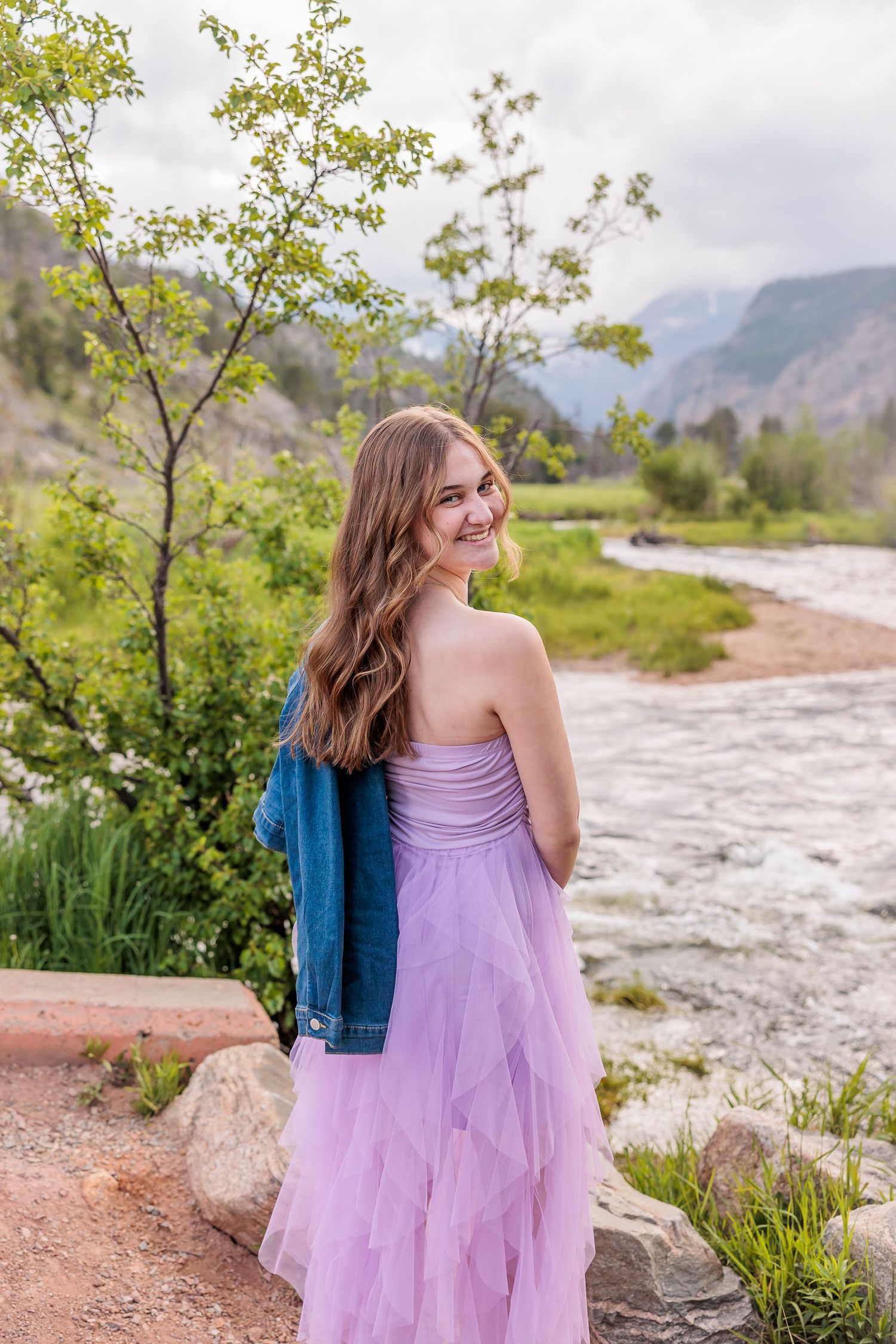 A purple dress flows in the breeze as mountains and a winding river create a scenic backdrop.