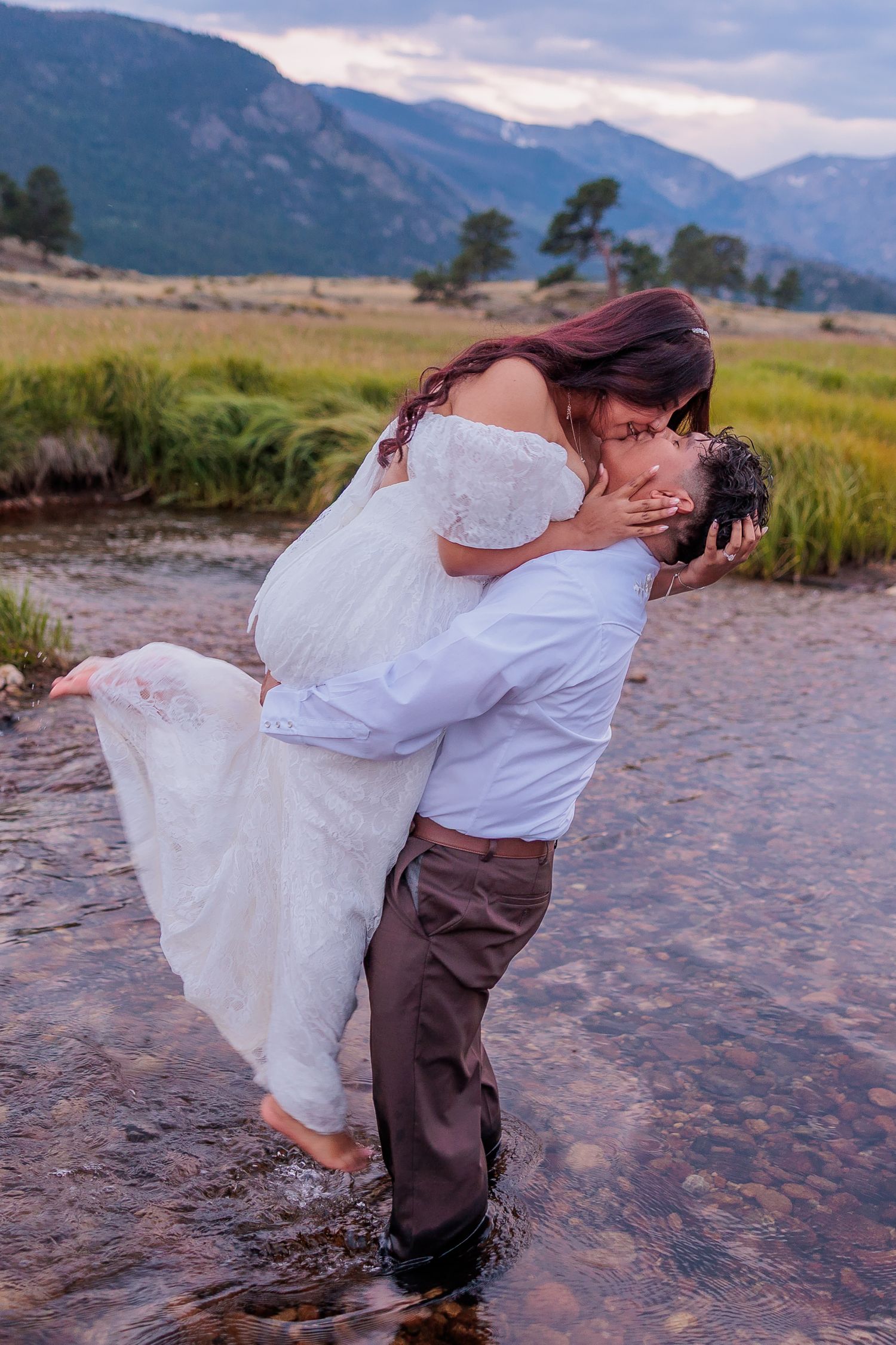 A romantic dip kiss in a mountain stream with flowing white dress and dramatic mountain backdrop.