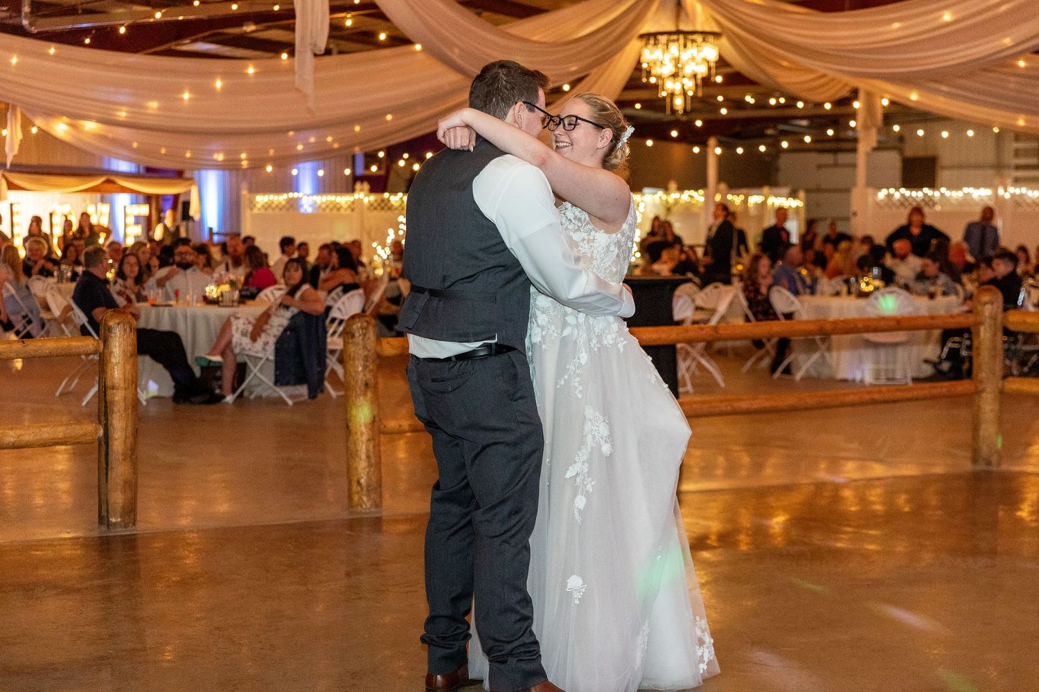 A couple shares a romantic dance at an elegant wedding reception under draped fabric and twinkling lights.