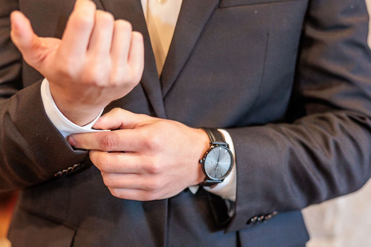 Business person in dark suit checking smartphone while sitting at desk with laptop and papers.