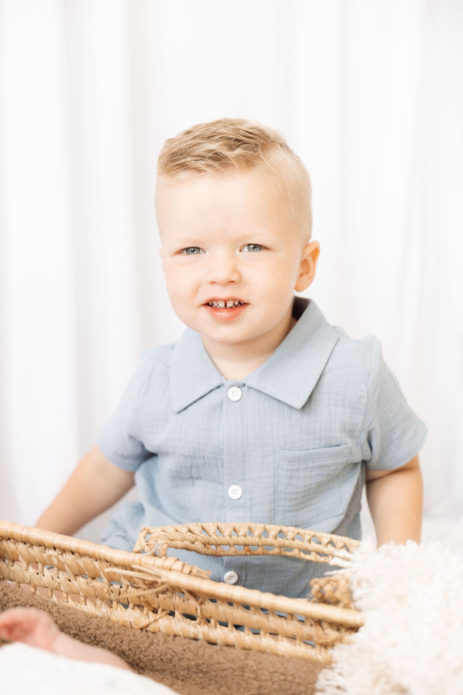 Smiling toddler boy in a blue shirt holding a wicker basket against a white background.