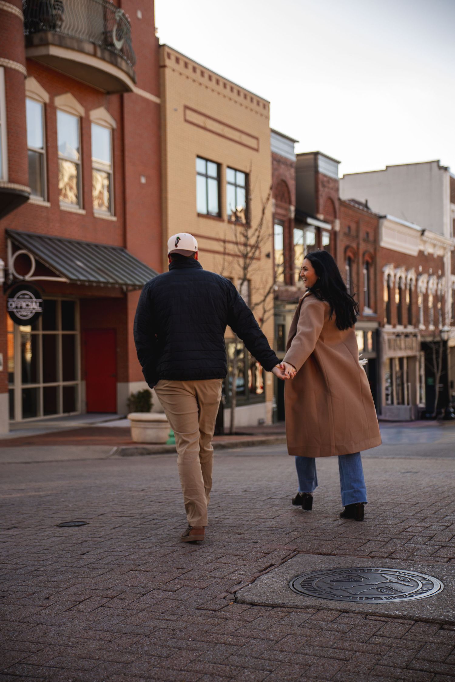 Couple walking hand in hand through historic brick downtown street.