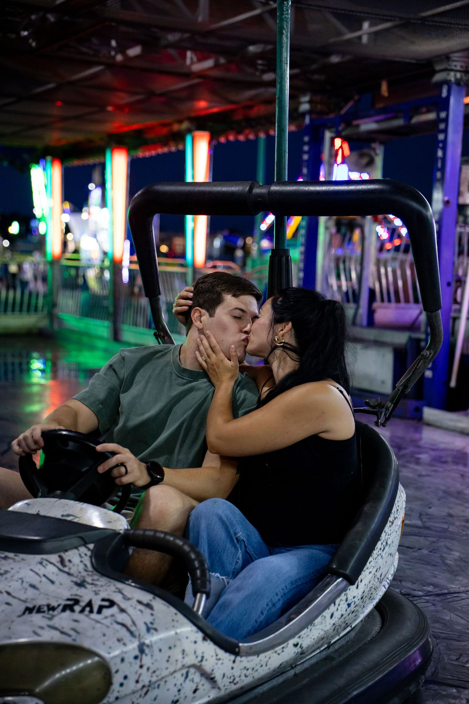 Couple sharing a romantic kiss on a bumper car ride at a colorful amusement park at night.