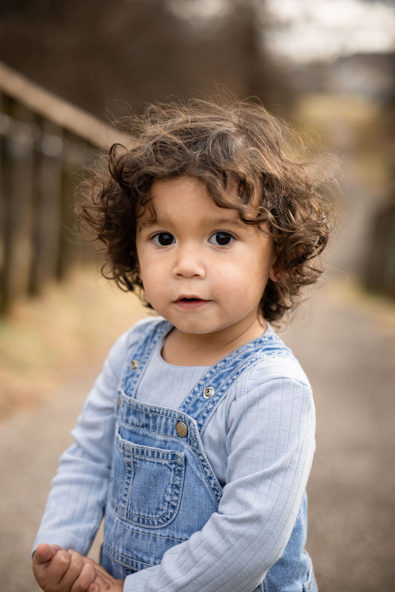 Toddler in denim overalls and striped shirt plays outdoors on path.