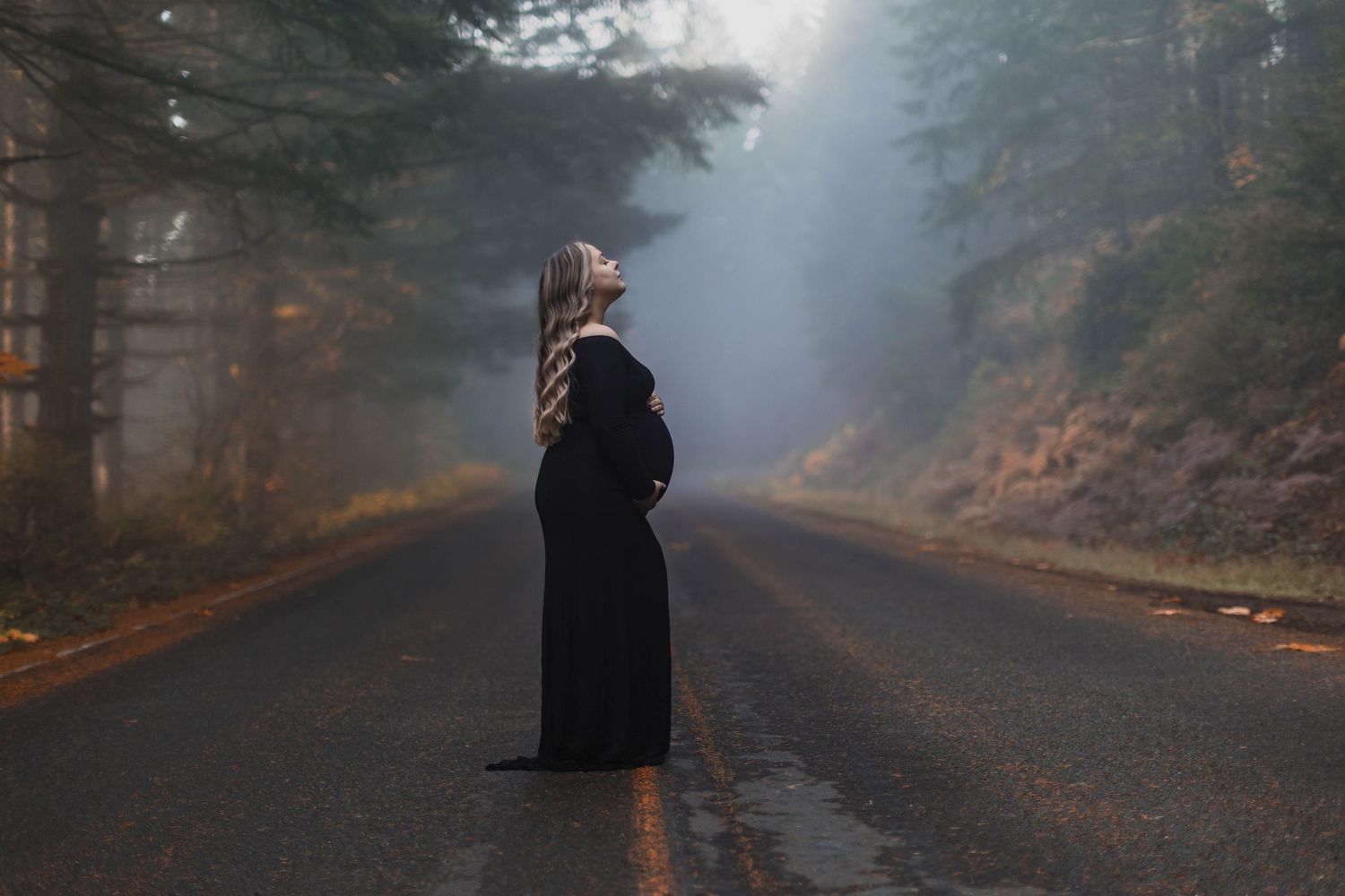 A dark foggy road through a forest creates an eerie and mysterious atmosphere.