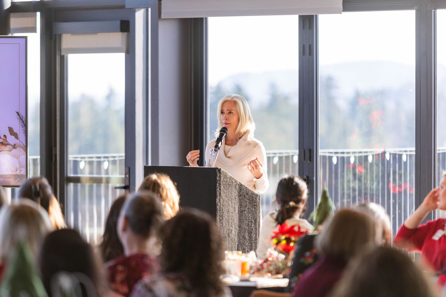 People gather around tables in a bright room with large windows for a social event or celebration.
