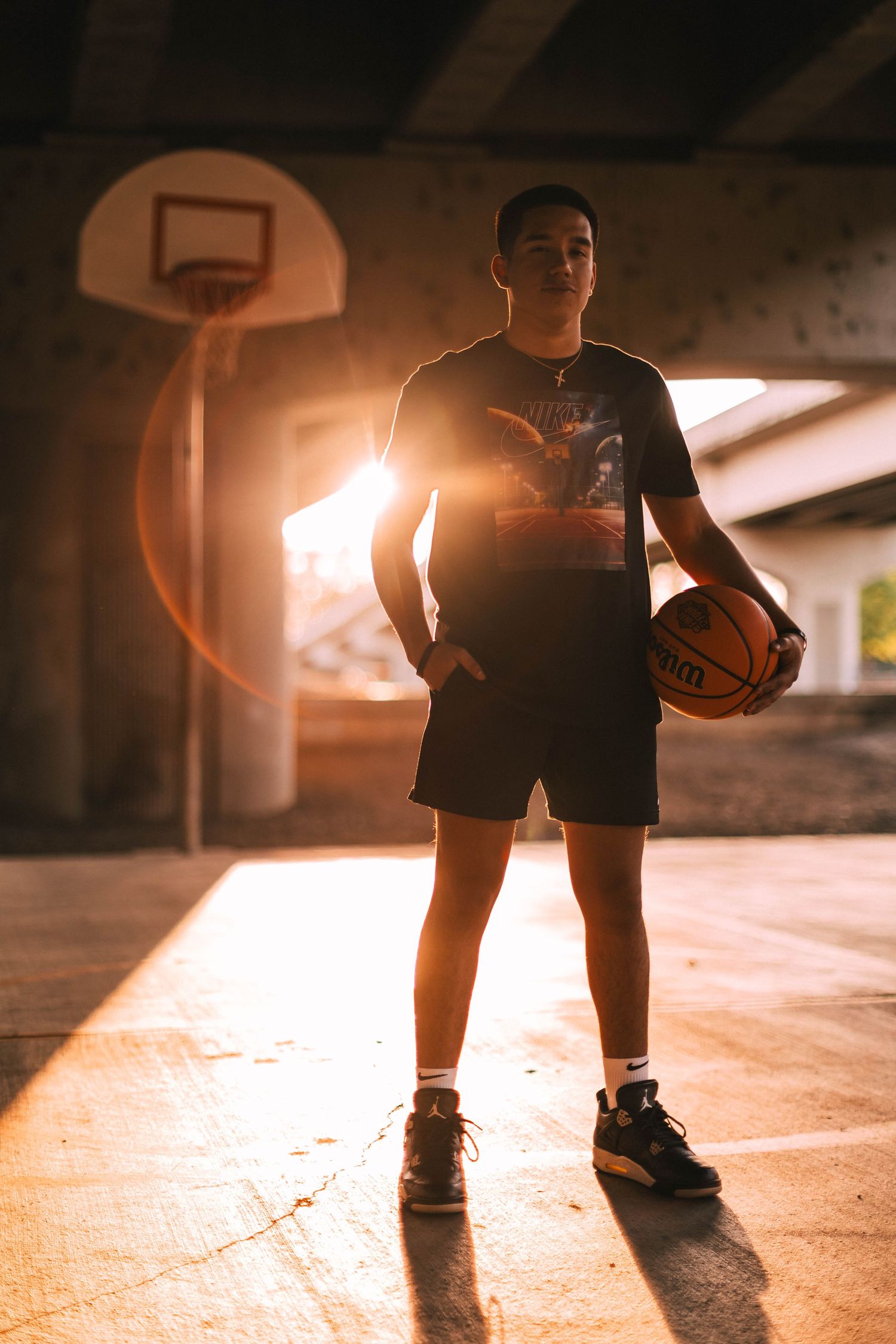 Basketball player practicing dribbling drills in a dimly lit indoor court at sunset.